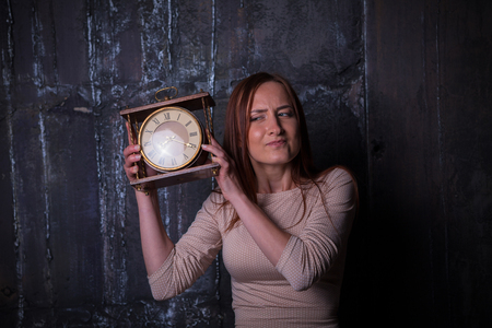 Pretty young woman holding a big clock. Faces series with different emotions.の写真素材