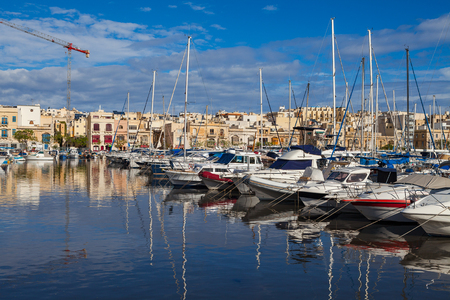 MSIDA, MALTA - OCTOBER 19, 2016: Many beautiful boats in small harbour with cityscape on the backgroundのeditorial素材