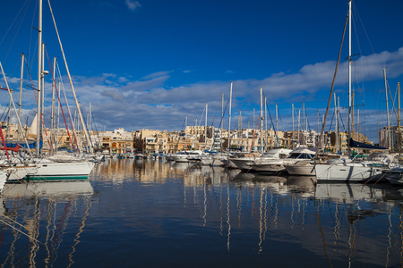 MSIDA, MALTA - OCTOBER 19, 2016: Many beautiful boats in small harbour with cityscape on the backgroundのeditorial素材