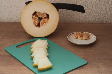 Black knife in fresh melon, sliced mllon on cutting board on wooden table