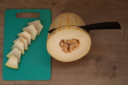 Black knife in fresh melon sliced on cutting board on wooden tableの写真素材