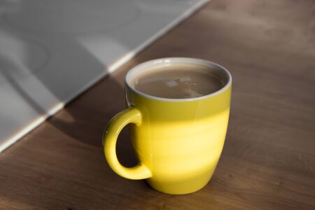 Yellow mug or cup of coffee on wooden table in the morning lightの写真素材