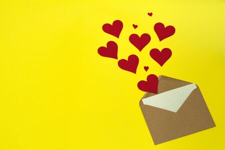 Red paper hearts fly out of craft paper envelope on the yellow background. Valentine day. love concept. Gift, message for lover. Space for text. Square banner.の写真素材