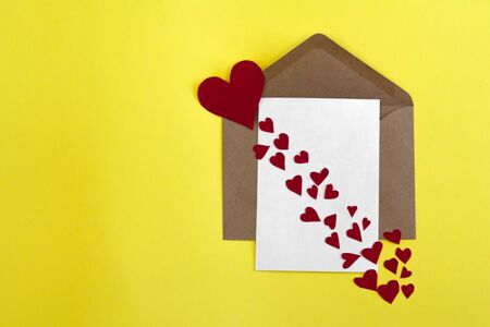 White card in craft envelope with red paper hearts and Cupid's arrow on yellow background.の写真素材
