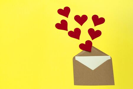 Red paper hearts fly out of craft paper envelope on the yellow background. Valentine day. love concept. Gift, message for lover. Space for text. Square banner.の写真素材