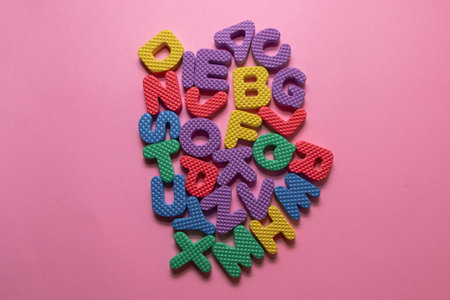 Colorful plastic alphabet letters on pink background, top view.