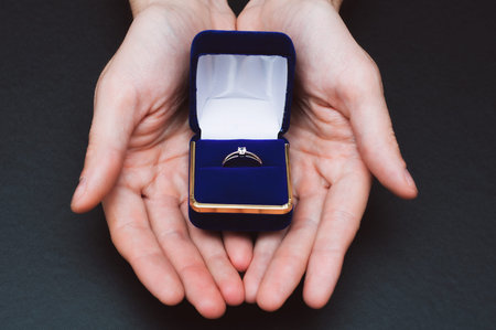 Man hands holding a blue box with a engagement rings.