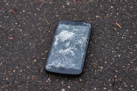 Phone with broken screen on asphalt. Someone dropped device