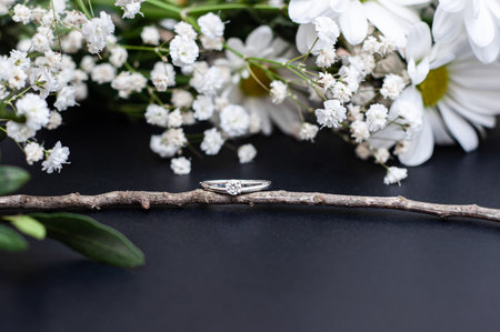 Wedding ring sitting on a tree branch with white flowers on a black background.