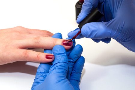 manicure specialist covers the nails with red varnish. close up