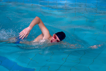 Man swims forward crawl style in swimming pool indoor