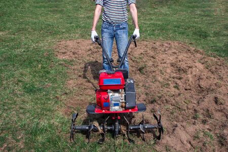 Man working in the garden with garden tiller. tractor cultivating and loosens soil field at springの写真素材