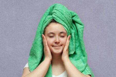 happy young girl with clean skin and with a green towel on her head puts hands to face. washesの写真素材