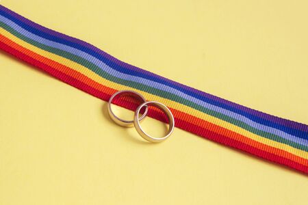 pair of white golden wedding rings on LGBTQ rainbow ribbon on yellow backgroundの写真素材