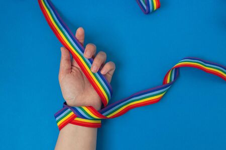 LGBT rainbow ribbon on hand on blue background. Concept of thanks to doctors during a pandemic and hope Let's all be wellの写真素材