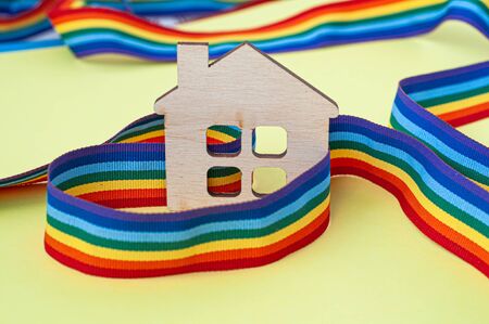 mini toy wooden house and lgbt rainbow ribbbon on yellow background, copy spaceの写真素材
