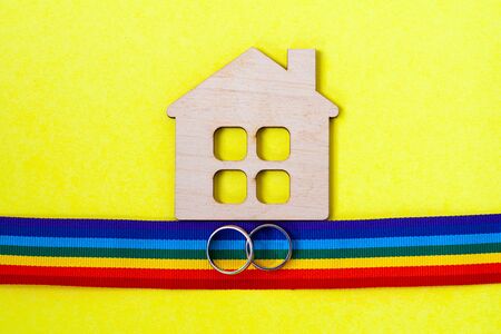 mini toy wooden house and lgbt rainbow ribbbon with rings on yellow background, top viewの写真素材