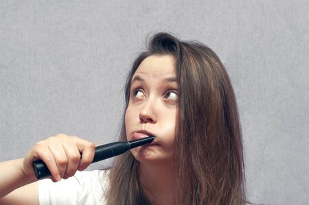 Pretty young girl with black electric brush cleaning teeth. Happy woman clean her oral cavity caring about dental health.の写真素材