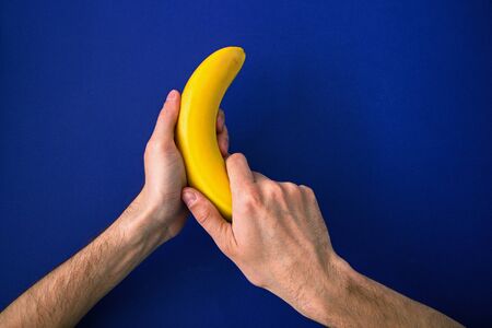 male hands holding a bright yellow banana on a blue backgroundの写真素材