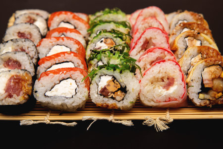 large sushi set with different maki - hosomaki, futomaki and uramaki on bamboo mate on a black background.の写真素材