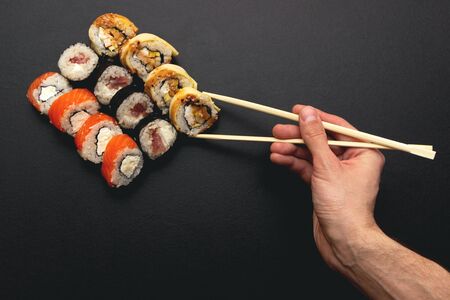 Sushi set on a black plate background. A male hand holds a roll of chopsticks. Top viewの写真素材