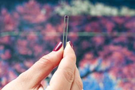 Girl collect diamond painting. Diamond embroidery with a tweezers. Acrylic rhinestones. Closeup,...