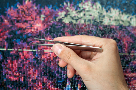 Male hand collect diamond painting. Diamond embroidery with a tweezers. Acrylic rhinestones. Closeup, selective focusの写真素材