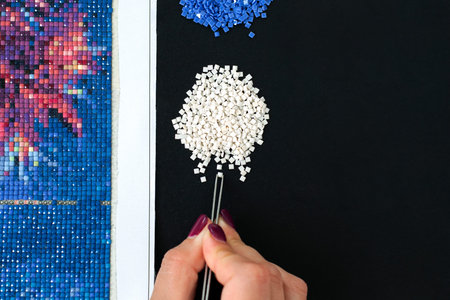 Girl hand collect diamond painting. Diamond embroidery with a tweezers. Acrylic rhinestones....