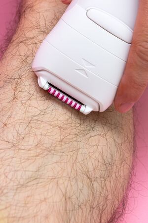 Man epilates his leg with an electric epilator device. close-up male fragment leg shaver shaving. Skin Care and Health. Hair Removal.の写真素材