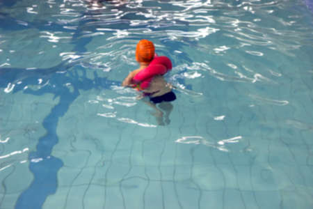 Cute little toddler boy child kicking feet in swimming costume use pool noodle and kickboard learn to swim at indoor pool, Swimming school for children conceptの写真素材