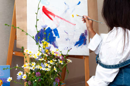 Creative pensive female painter paints a colorful abstract picture. Closeup of painting process in art workshopの写真素材