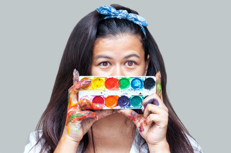 Happy woman hiding the face with her painted hand and paints . Creative, art, drawing conceptの写真素材