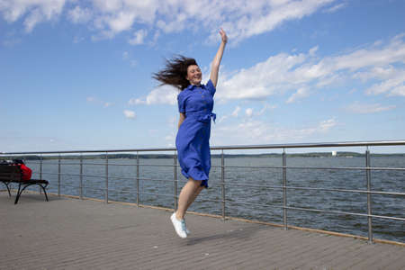Portrait of happy beautiful young woman jumping on the pier. Caucasian female enjoying a sunny day at the sea shore. Freedom conceptの写真素材