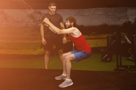 Young man performing  training in gym with personal coach. Sporty male doing stretching exercise...