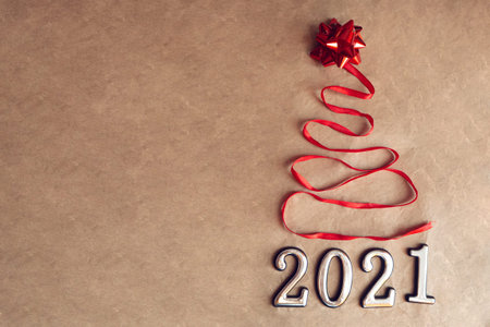 Beautiful christmas tree made from red satin ribbon and star and 2021 on craft brown background with...