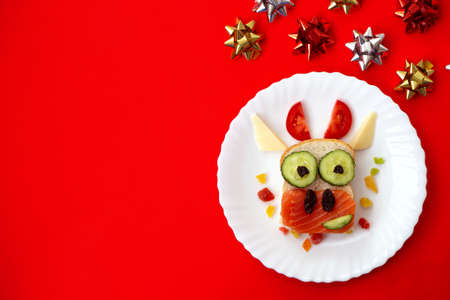 Funny sandwich with edible symbol of 2021 bull cow made from toast bread, red fish, cucumber, tomato, cheese and raisins. Breakfast idea for kids. christmas food top view. food art with copy spaceの写真素材