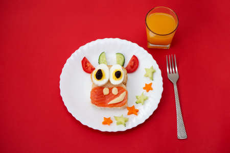 Funny sandwich with edible symbol of 2021 bull cow made from toast bread, red fish, cheese, raisins, eggs, vegetables and juice. Breakfast idea for kids. christmas food top view. food artの写真素材