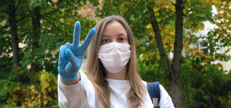 Outdoors portrait of beautiful young woman wearing cotton white mask and medicalgloves greeting and...