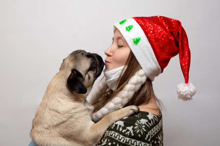 Woman in medical mask and Christmas hat kissing with pug dog. Coronavirus and Christmas concept.の写真素材
