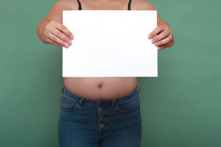 Overweight fat woman showing her belly fat with paper with copy space, selective focus. Bodysitive...