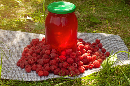 Raspberry drink in jar and ripe raspberry outside on green leaf and sunlight background
