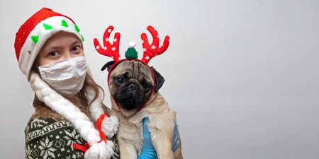 Woman in medical mask and Christmas hat with pug dog in traditional red Christmas deer. Coronavirus and Christmas concept. pet with owner, isolationの写真素材