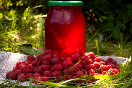 Raspberry drink in jar and ripe raspberry outside on green leaf and sunlight background