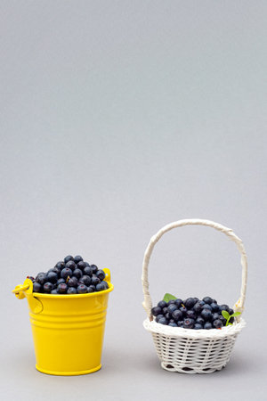 yellow bucket and wicker white basket of ripe blueberry with green leaf on white backgroundの写真素材