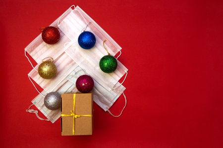 Flat lay with Christmas tree made from medical masks, balls and gift box, on red background with copy space. Merry christmasの写真素材
