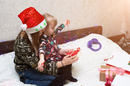 woman and kid girl packaging Christmas gifts for friends and family. mom wearing red Santa Claus hat with child in deer antlers have fun, play, preparation for xmas holidays. cozy celebration concept.の写真素材