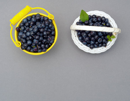 yellow bucket and wicker white basket of ripe blueberry with green leaf on white background, close upの写真素材