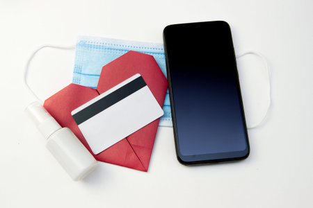 red paper heart with smartphone, medical mask, sanitizer and credit card. Concept of online Dating, love and relationships and gifts in quarantine and Covid-19. St. Valentines dayの写真素材