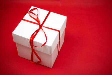 Single white gift box with red ribbon on red background with copy spaceの写真素材