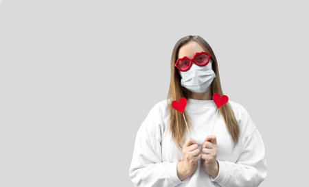 Portrait of woman in funny glasses and medical protective wearing mask holding in hands red hearts....